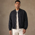 Man wearing raw indigo denim bomber jacket over a jumper with dark trousers