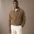 Man wearing tan suede aviator jacket over a plain tee with dark denim