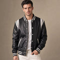 Man wearing a black sheepskin varsity jacket over a sweatshirt with dark denim